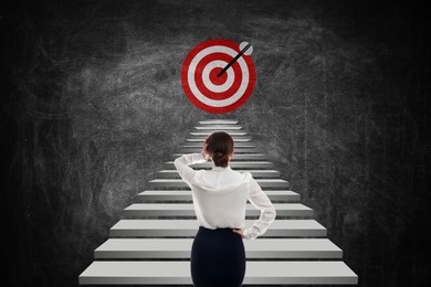 Image of Targeting, goal achievement. Business woman walking up stairs leading to bullseye with arrow