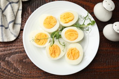 Photo of Boiled eggs and microgreens on wooden table, flat lay