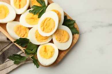 Photo of Boiled eggs and parsley on white marble table, top view. Space for text