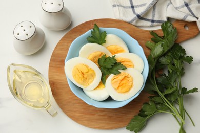 Photo of Boiled eggs, parsley and oil on white marble table, flat lay