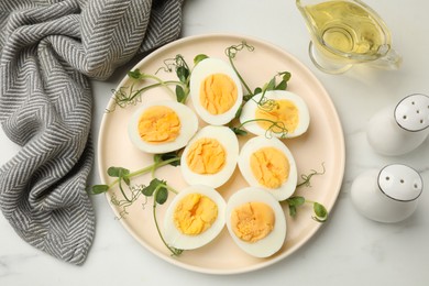 Photo of Boiled eggs, microgreens and oil on white marble table, flat lay