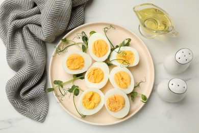 Photo of Boiled eggs, microgreens and oil on white marble table, flat lay