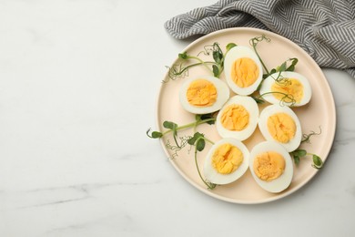 Photo of Boiled eggs, microgreens and oil on white marble table, top view. Space for text