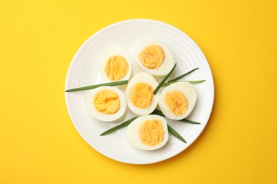 Photo of Boiled eggs and green onions on yellow background, top view