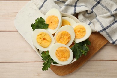 Photo of Boiled eggs and parsley in bowl on wooden table, top view