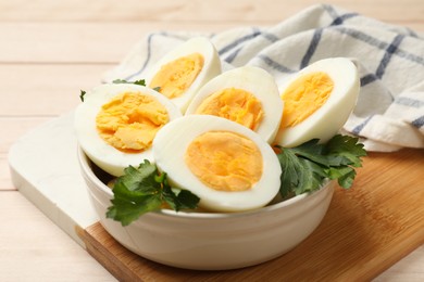 Photo of Boiled eggs and parsley in bowl on wooden table, closeup