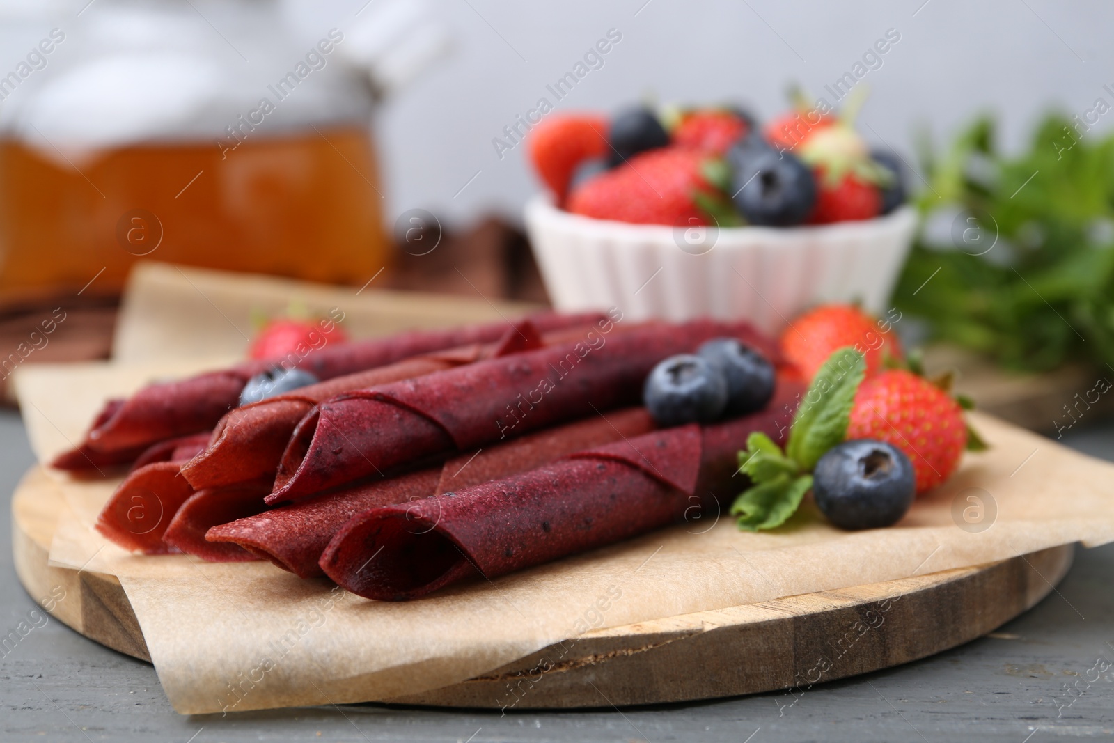 Tasty fruit leather rolls, strawberries, blueberries and mint on grey wooden table, closeup Photo of Tasty fruit leather rolls, strawberries, blueberries and mint on grey wooden table, closeup