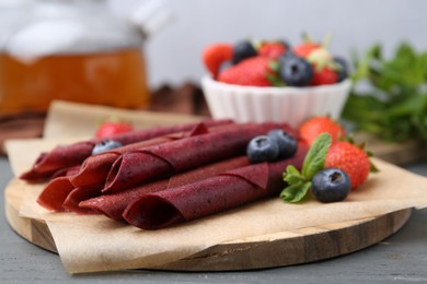 Photo of Tasty fruit leather rolls, strawberries, blueberries and mint on grey wooden table, closeup