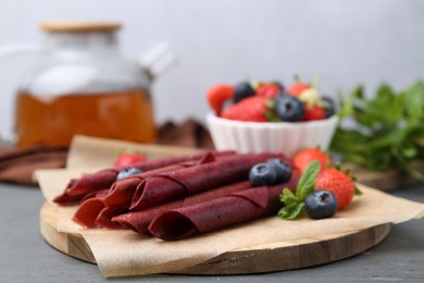 Photo of Tasty fruit leather rolls, strawberries, blueberries and mint on grey wooden table, closeup