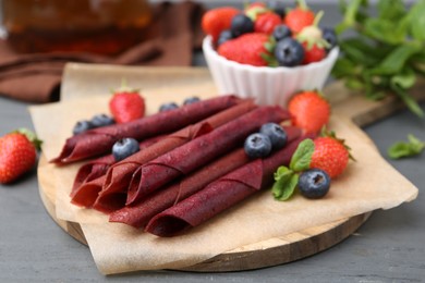 Photo of Tasty fruit leather rolls, strawberries, blueberries and mint on grey wooden table, closeup