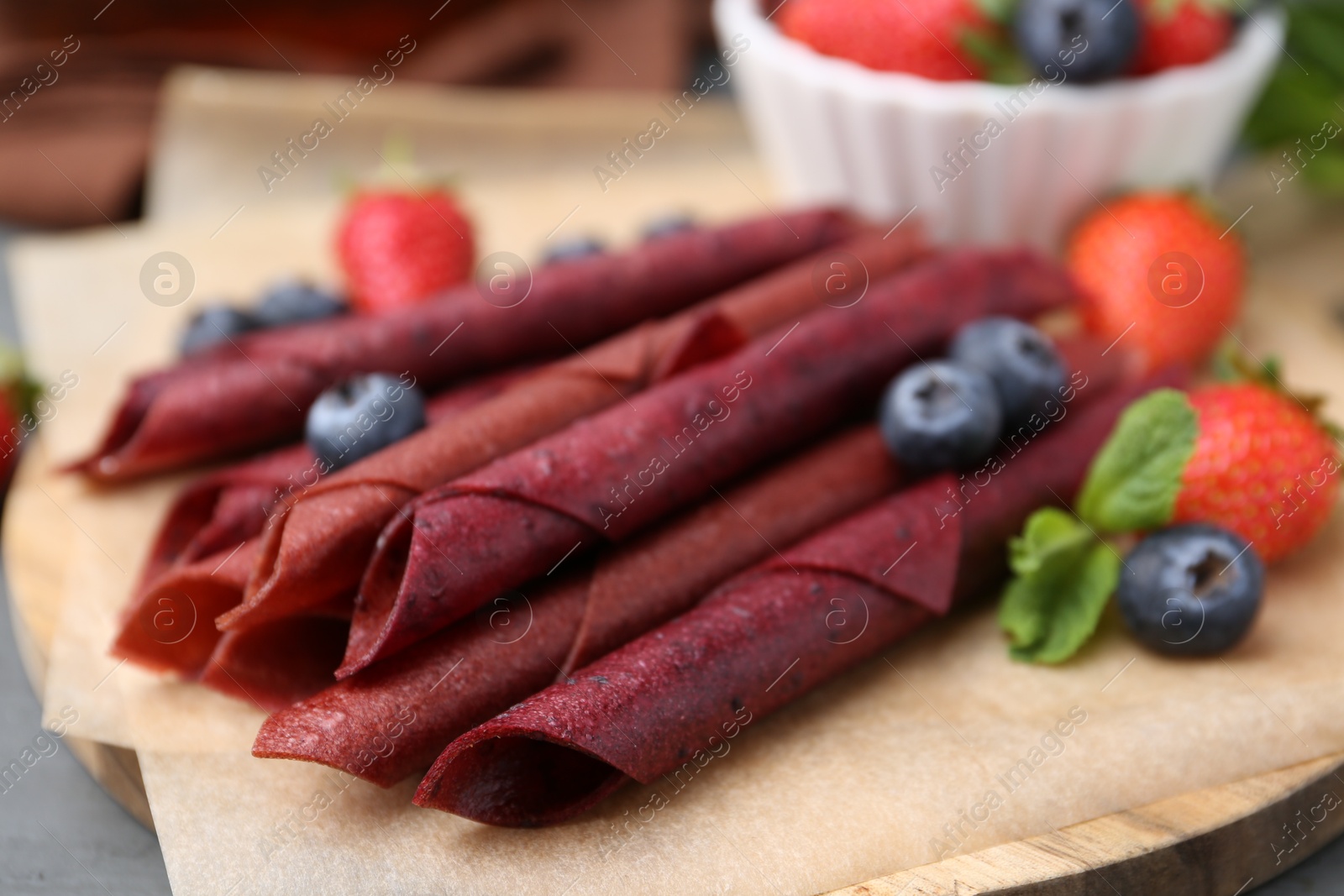 Tasty fruit leather rolls, strawberries, blueberries and mint on grey wooden table, closeup Photo of Tasty fruit leather rolls, strawberries, blueberries and mint on grey wooden table, closeup