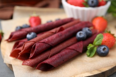 Photo of Tasty fruit leather rolls, strawberries, blueberries and mint on grey wooden table, closeup