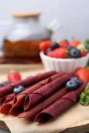 Photo of Tasty fruit leather rolls, strawberries, blueberries and mint on table, closeup