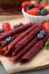 Photo of Tasty fruit leather rolls, strawberries, blueberries and mint on grey wooden table, closeup