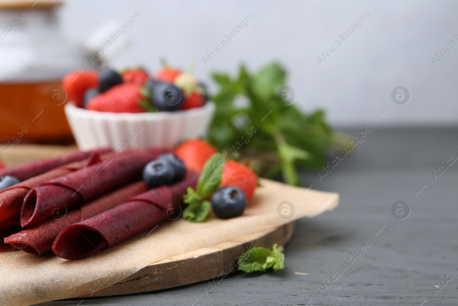 Tasty fruit leather rolls, strawberries, blueberries and mint on grey wooden table, closeup. Space for text Photo of Tasty fruit leather rolls, strawberries, blueberries and mint on grey wooden table, closeup. Space for text