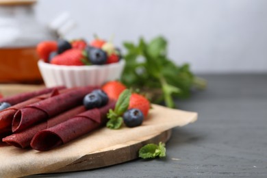 Photo of Tasty fruit leather rolls, strawberries, blueberries and mint on grey wooden table, closeup. Space for text