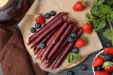 Photo of Tasty fruit leather rolls, strawberries, blueberries and mint on grey wooden table, flat lay