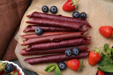 Photo of Tasty fruit leather rolls, strawberries, blueberries and mint on grey wooden table, flat lay