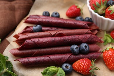 Photo of Tasty fruit leather rolls, strawberries, blueberries and mint on table, closeup