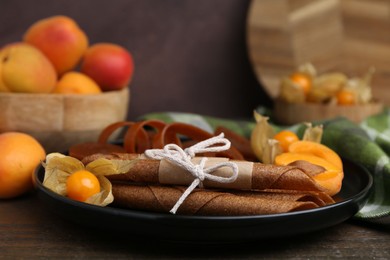 Photo of Tasty fruit leather, physalis and apricots on wooden table, closeup