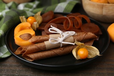 Photo of Tasty fruit leather, physalis and apricots on wooden table, closeup