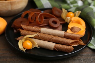 Photo of Tasty fruit leather, physalis and apricots on wooden table, closeup