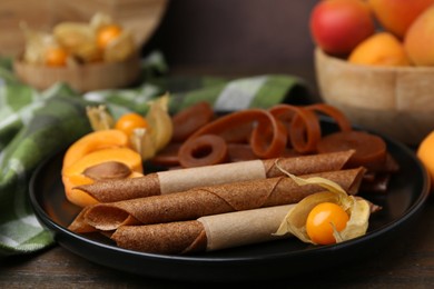 Photo of Tasty fruit leather, physalis and apricots on wooden table, closeup