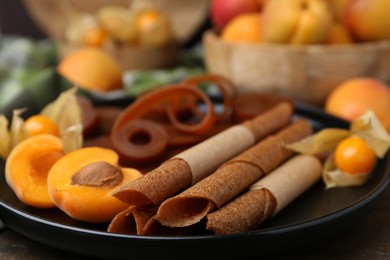 Photo of Tasty fruit leather, physalis and apricots on wooden table, closeup