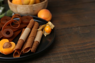 Photo of Tasty fruit leather, physalis and apricots on wooden table, closeup. Space for text