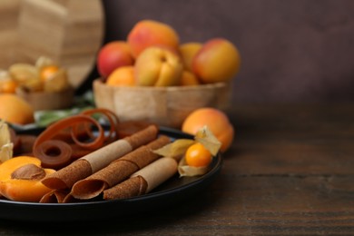 Photo of Tasty fruit leather, physalis and apricots on wooden table, closeup. Space for text