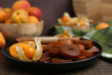 Photo of Tasty fruit leather, physalis and apricots on wooden table, closeup