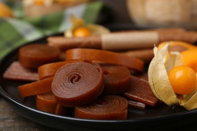 Photo of Tasty fruit leather and physalis on wooden table, closeup