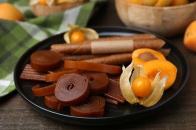 Photo of Tasty fruit leather, physalis and apricots on wooden table, closeup