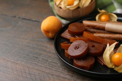 Photo of Tasty fruit leather, physalis and apricots on wooden table, closeup. Space for text