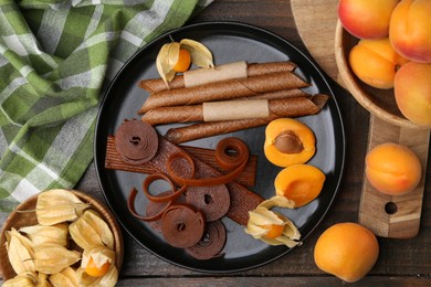 Photo of Tasty fruit leather, physalis and apricots on wooden table, flat lay