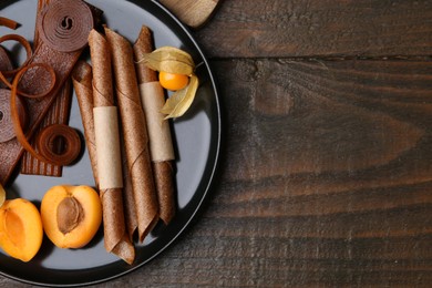 Photo of Tasty fruit leather, physalis and apricots on wooden table, top view. Space for text