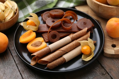 Photo of Tasty fruit leather, physalis and apricots on wooden table, closeup