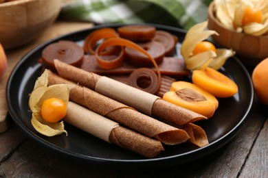 Photo of Tasty fruit leather, physalis and apricots on wooden table, closeup