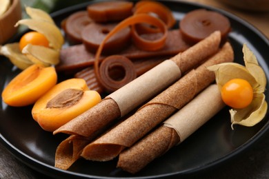 Photo of Tasty fruit leather, physalis and apricots on wooden table, closeup