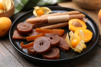 Photo of Tasty fruit leather, physalis and apricots on wooden table, closeup