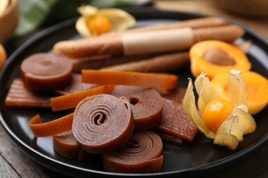 Photo of Tasty fruit leather, physalis and apricots on wooden table, closeup