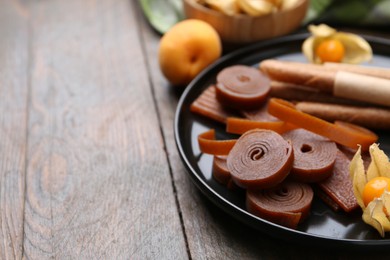 Photo of Tasty fruit leather, physalis and apricots on wooden table, closeup. Space for text