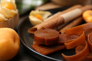Photo of Tasty fruit leather and apricots on wooden table, closeup