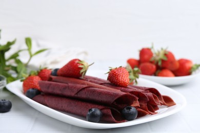 Photo of Tasty fruit leather rolls, strawberries and blueberries on white table, closeup. Space for text
