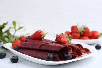 Photo of Tasty fruit leather rolls, strawberries and blueberries on white table, closeup. Space for text