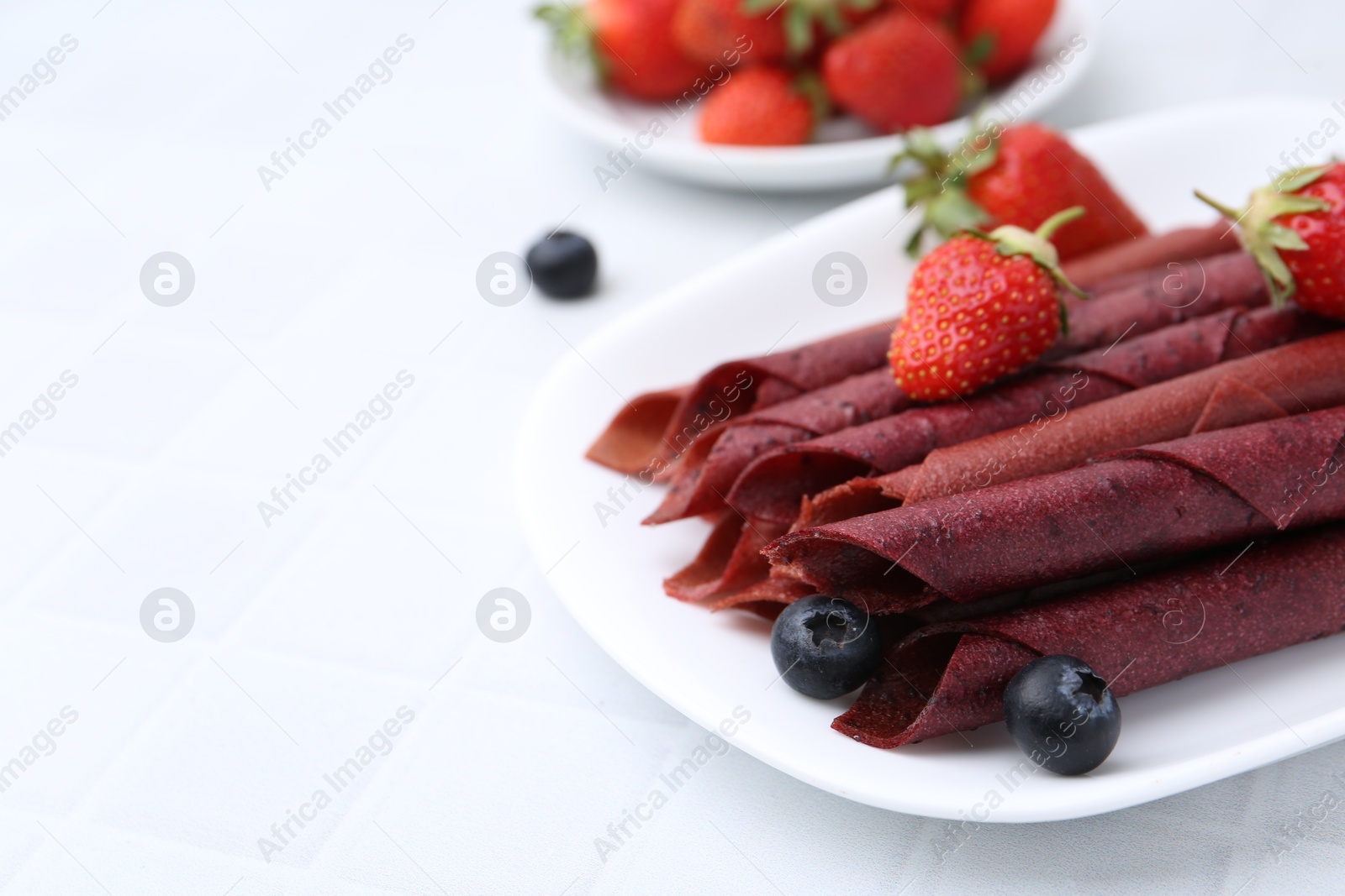 Tasty fruit leather rolls, strawberries and blueberries on white table, closeup. Space for text Photo of Tasty fruit leather rolls, strawberries and blueberries on white table, closeup. Space for text