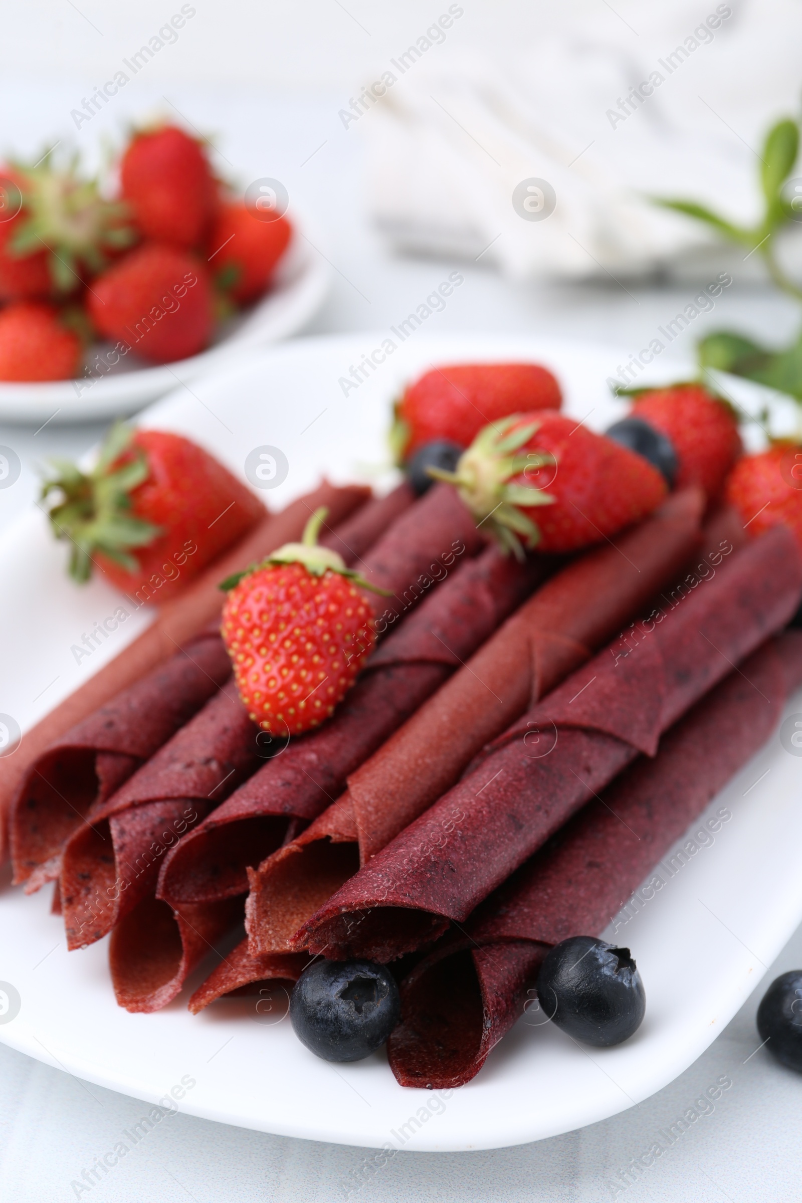 Tasty fruit leather rolls, strawberries and blueberries on white table, closeup Photo of Tasty fruit leather rolls, strawberries and blueberries on white table, closeup