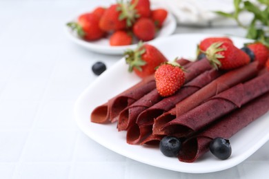Photo of Tasty fruit leather rolls, strawberries and blueberries on white table, closeup. Space for text