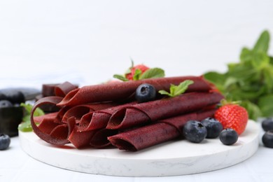 Photo of Tasty fruit leather rolls, strawberries, blueberries and mint on white table, closeup