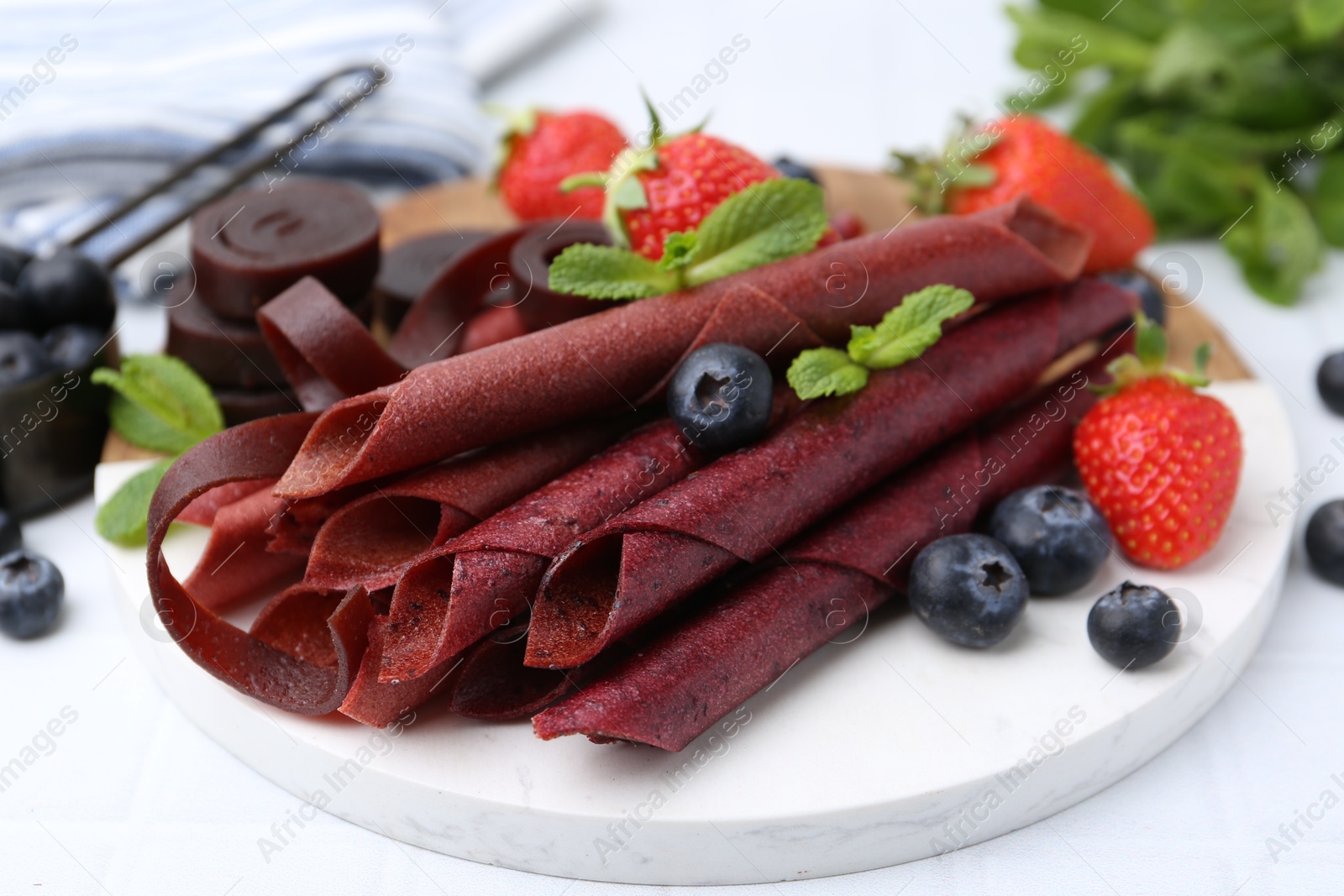 Tasty fruit leather rolls, strawberries, blueberries and mint on white table, closeup Photo of Tasty fruit leather rolls, strawberries, blueberries and mint on white table, closeup